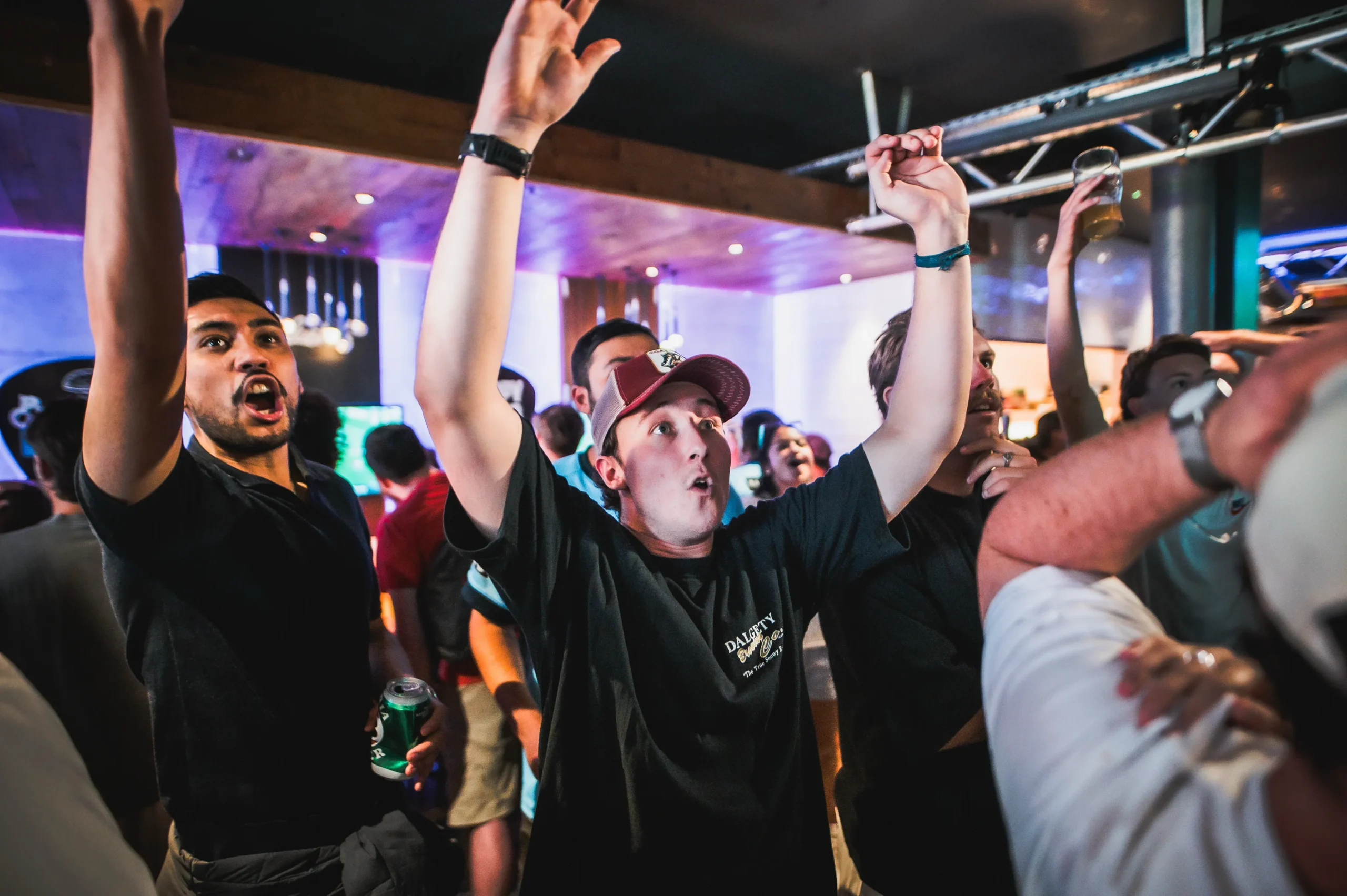 Packed crowd at Belushi's sports bar with arms raised watching the World Cup live, the electric atmosphere that only a room full of passionate football fans can generate