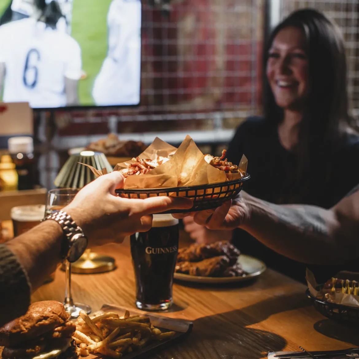 Friends sharing loaded bar food and drinks at Belushi's sports bar while watching the World Cup live on screen