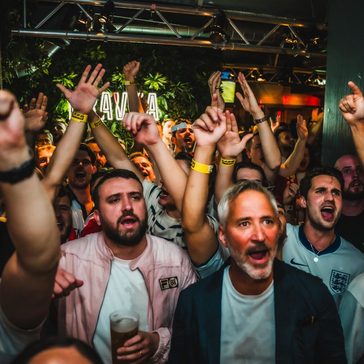 England football supporters singing and raising their hands during a World Cup 2026 match at Belushi's London, capturing the electric atmosphere of a live sports screening with a cold pint in hand